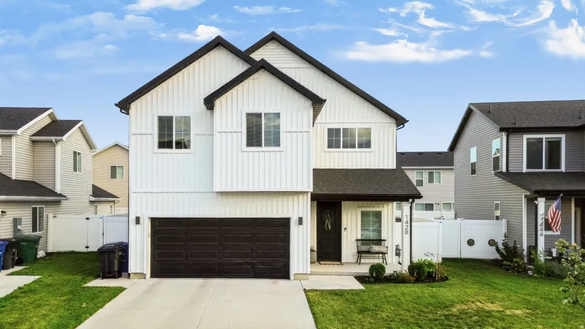Contemporary exterior featuring white board and batten siding, black trim accents, a two-car garage, concrete driveway, and a covered front porch