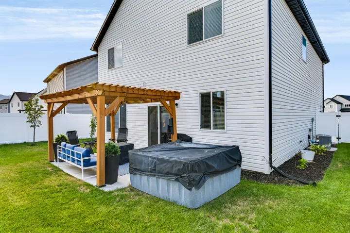 Expansive lawn featuring a concrete patio with a wood pergola, privacy fencing, and a spa