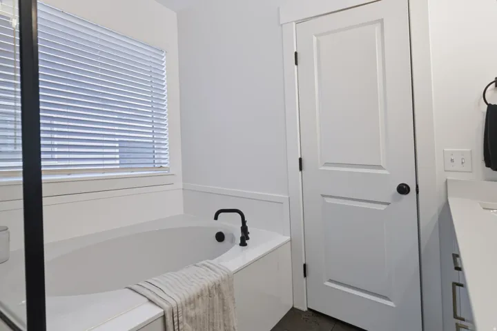 Built-in soaking tub with matte black fixtures, white window blinds, and paneled white door