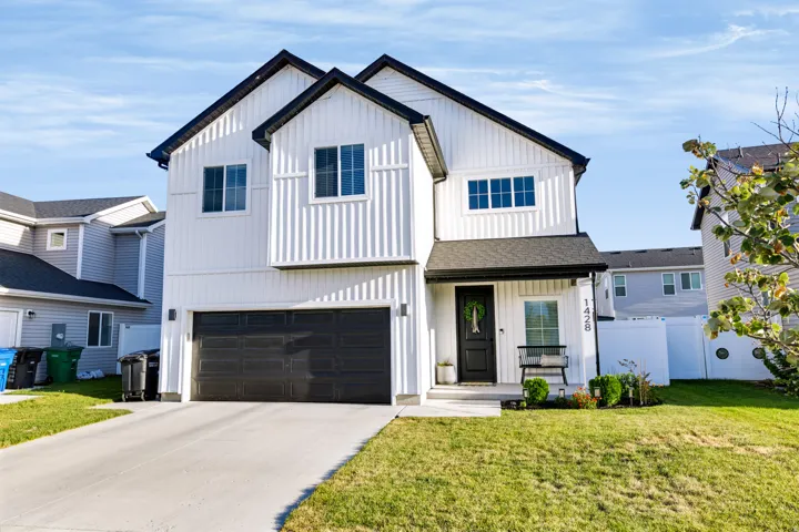 Modern farmhouse exterior featuring vertical white siding, black-trimmed windows, a dark shingled roof, an attached two-car garage, and a concrete driveway