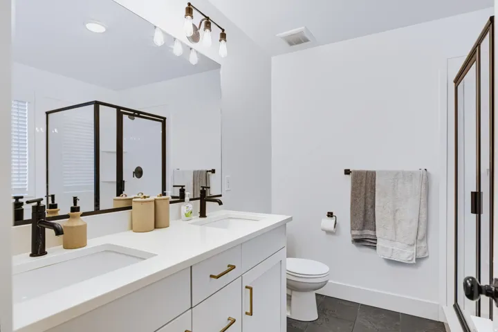 Dual vanity with integrated sinks, white quartz countertop, black-framed glass shower enclosure, matte black fixtures, and dark tile flooring