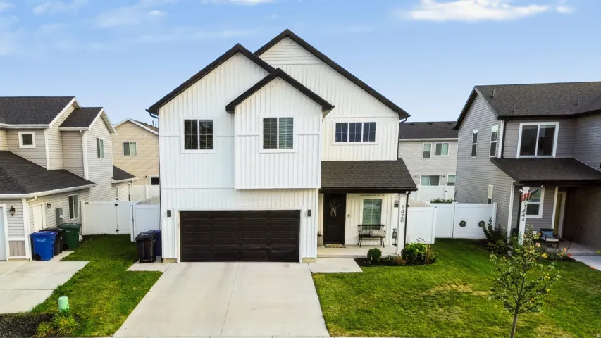 Two-story residence featuring white board-and-batten siding with black trim, an attached two-car garage, a covered entry porch, and a manicured front lawn