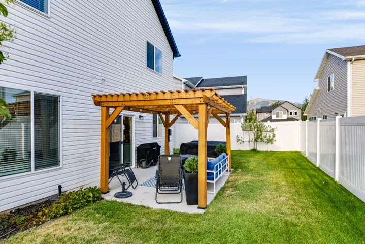 Private backyard featuring a concrete patio, wooden pergola, and a white privacy fence