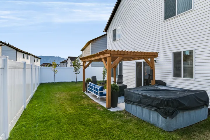 Expansive backyard featuring a manicured lawn, a white privacy fence, and a wooden pergola over a patio