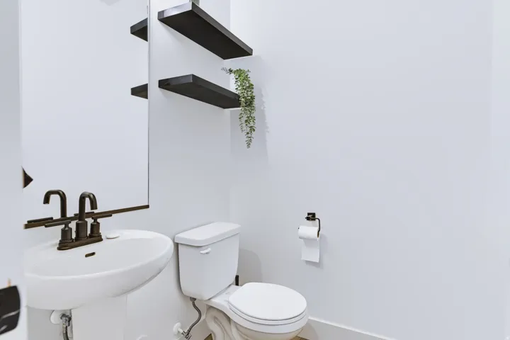 Pedestal sink with dark bronze faucet, wall-mounted mirror, and floating shelves