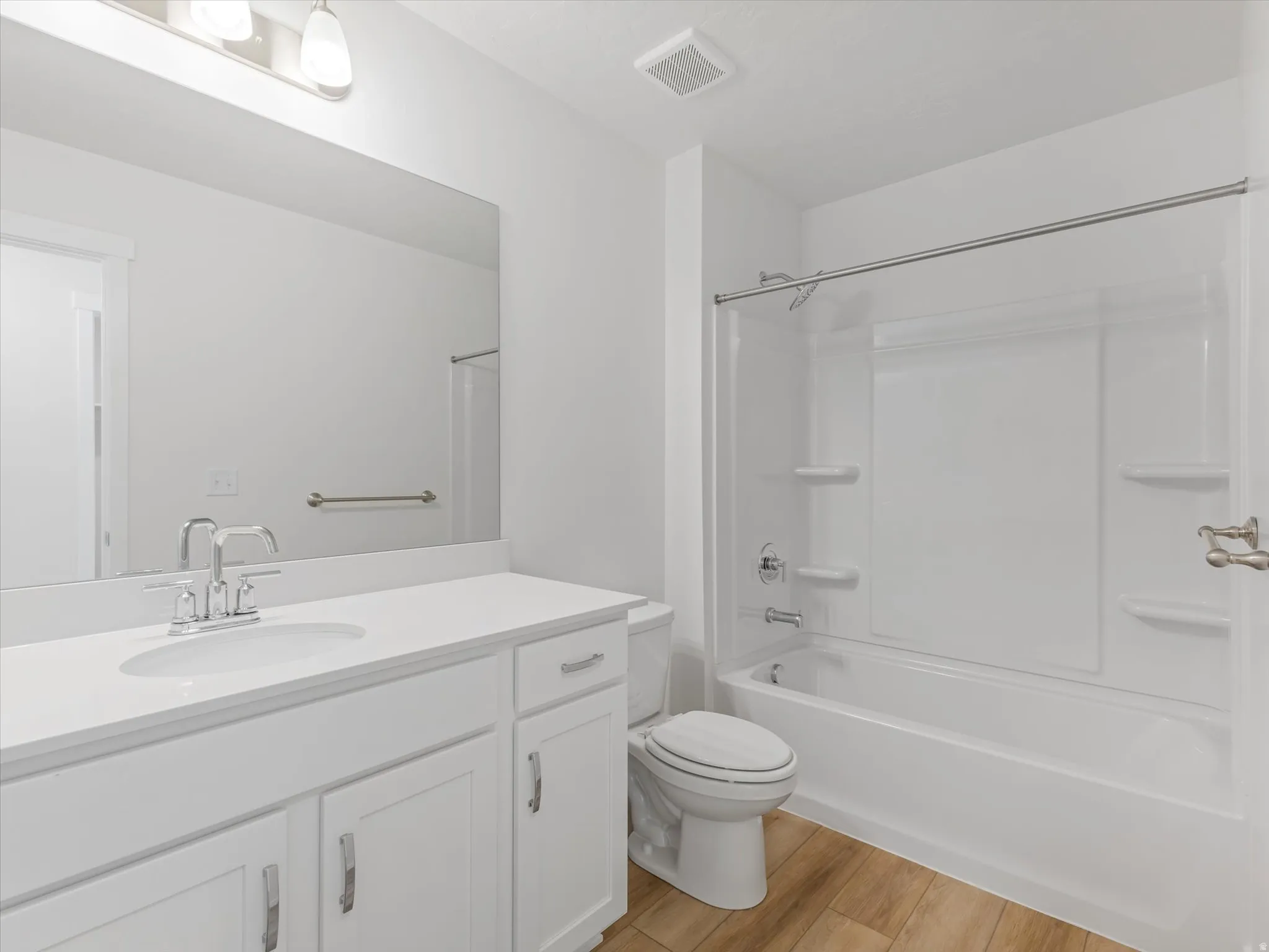 White vanity with chrome fixtures and integrated sink, white tub with shower, and wood-finish flooring