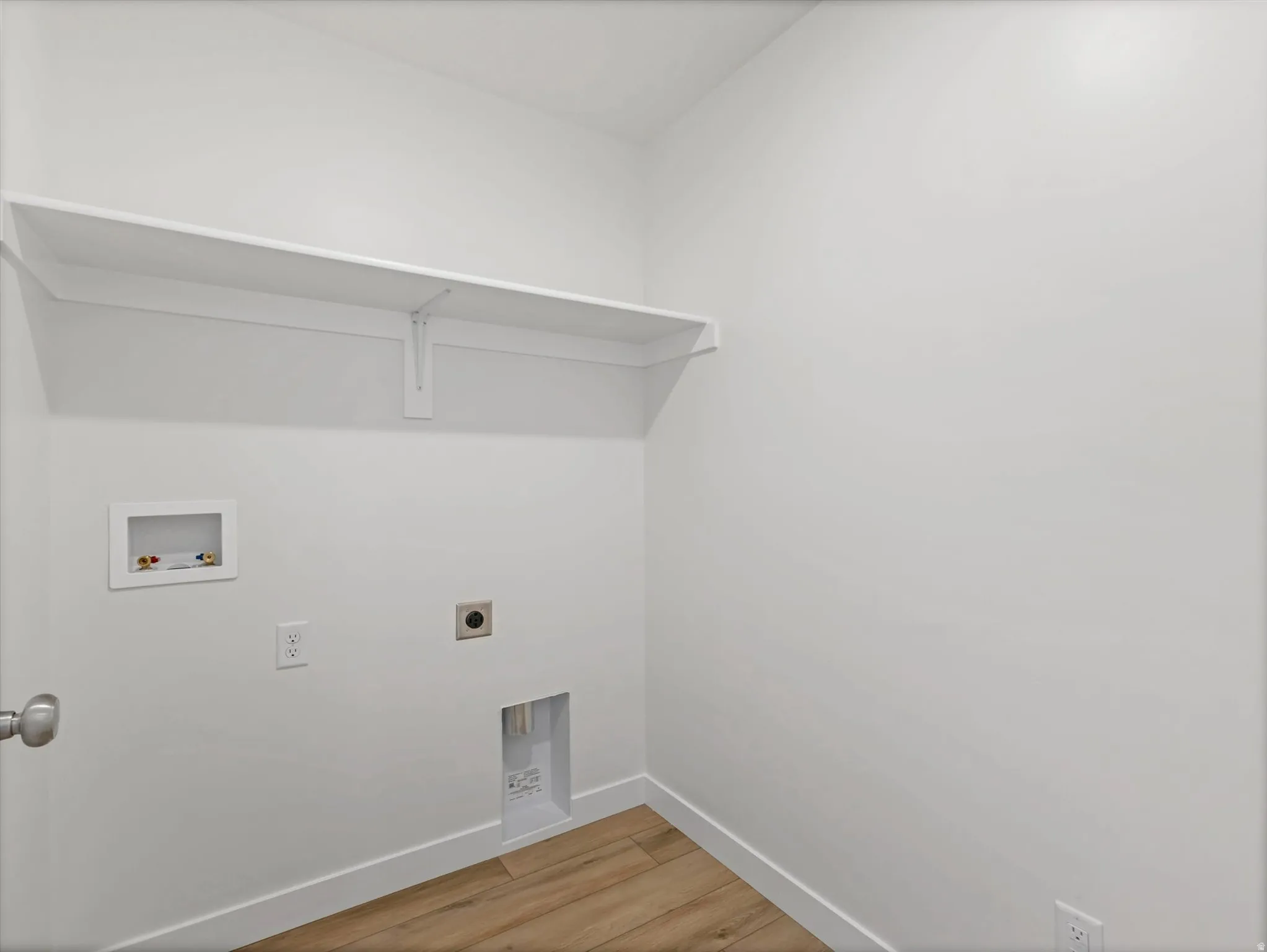 Dedicated utility space featuring a built-in white shelf, light wood-finish flooring, and white walls