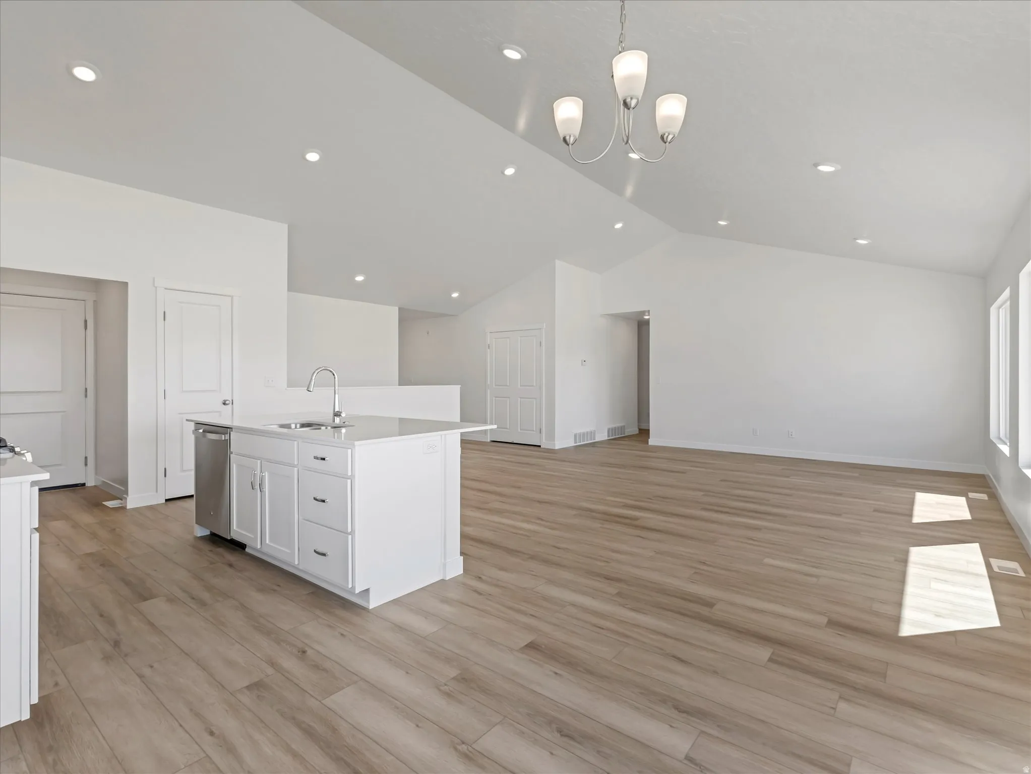 Open-concept living space featuring wood-finish flooring, vaulted ceilings, recessed lighting, a modern chandelier, and an island with stainless steel appliances