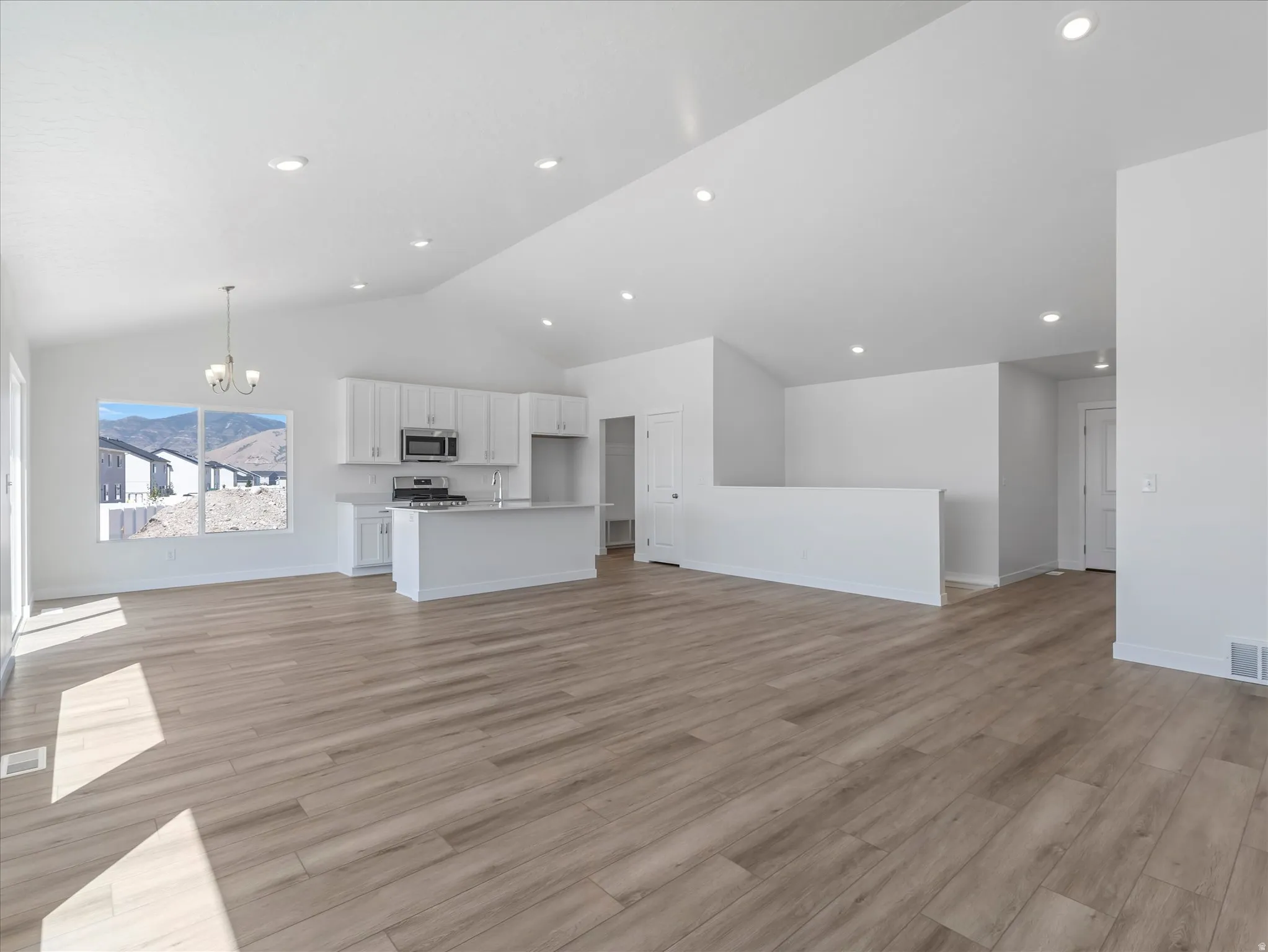 Open-concept living space featuring wood-finish flooring, vaulted ceilings, recessed lighting, and a modern kitchen with a large island and stainless steel appliances