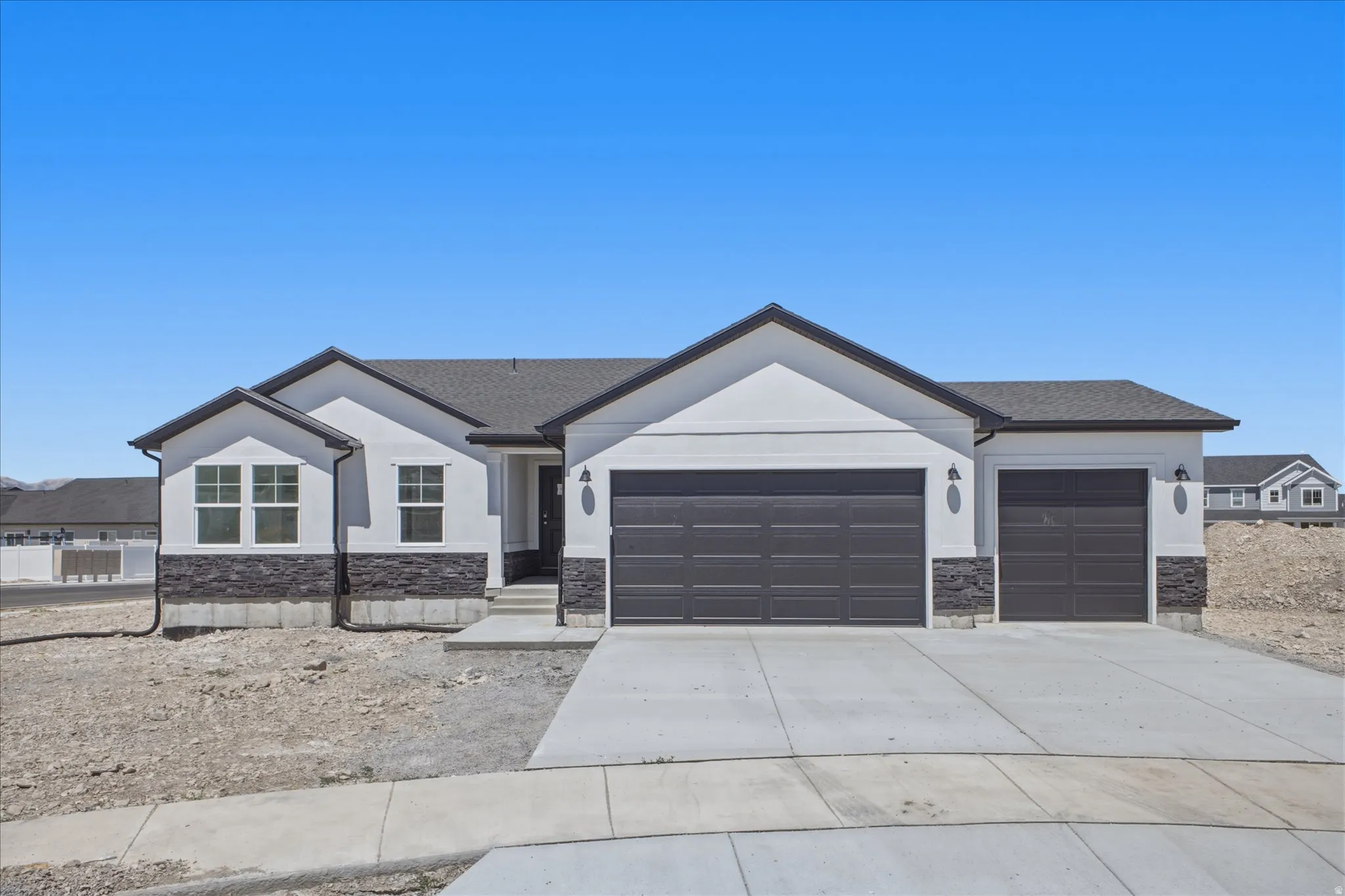 White stucco exterior with dark stone accents, a dark shingle roof, and a multi-car garage with panel doors