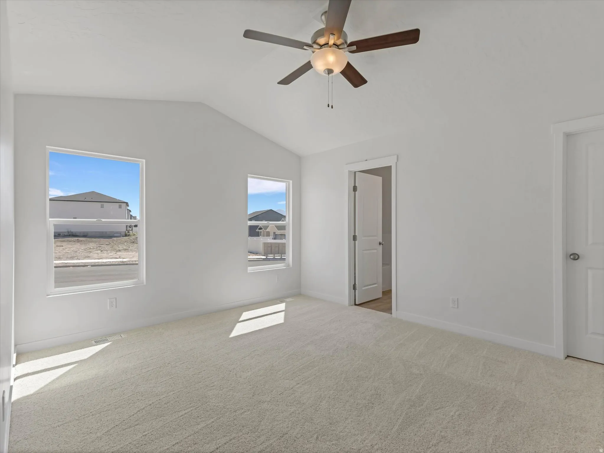 Vaulted ceiling with a ceiling fan, two windows, wall-to-wall carpeting, and white interior doors
