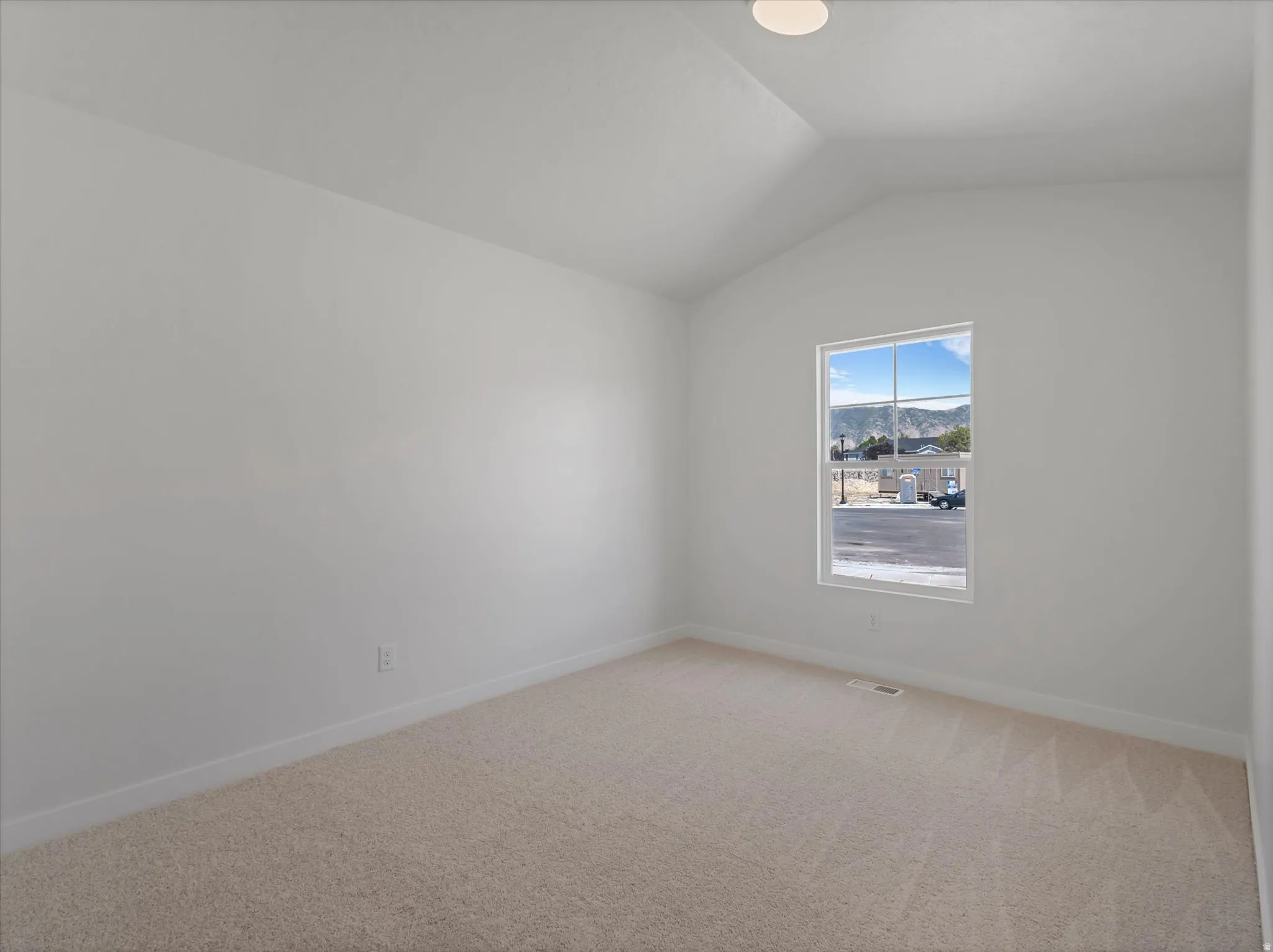 Vaulted ceiling room with neutral carpet, a single window, and a flush-mount ceiling light