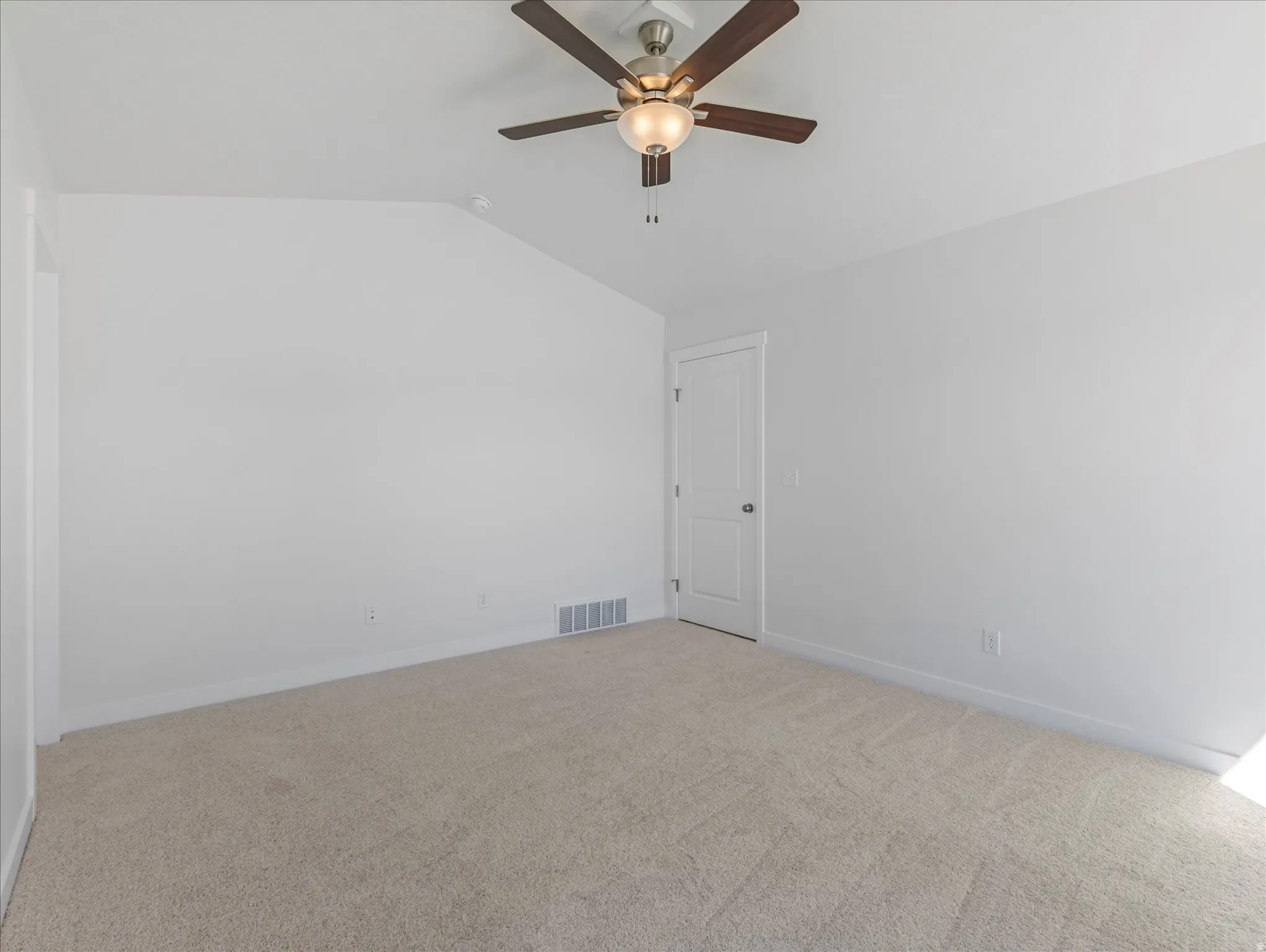 Textured carpet flooring, ceiling fan with integrated lighting, clean white walls, and a white door with dark hardware