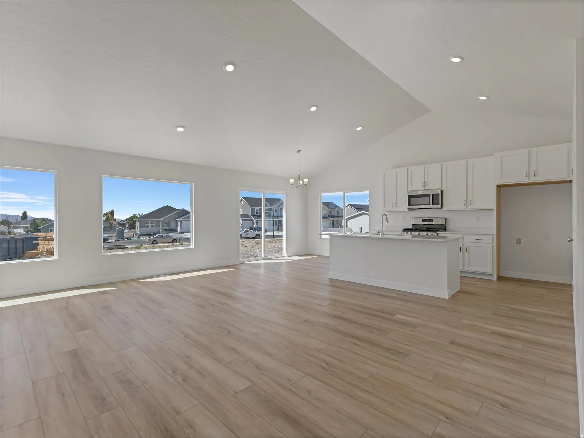 Vaulted ceilings with recessed lighting, wood-finish flooring, white kitchen cabinetry with stainless steel appliances, and a central kitchen island