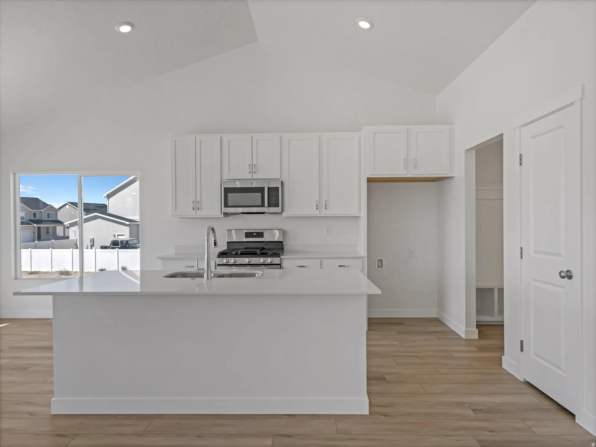 Open-concept kitchen with vaulted ceiling and recessed lighting, featuring an island with a stainless steel sink, stainless steel appliances, and wood-finish flooring