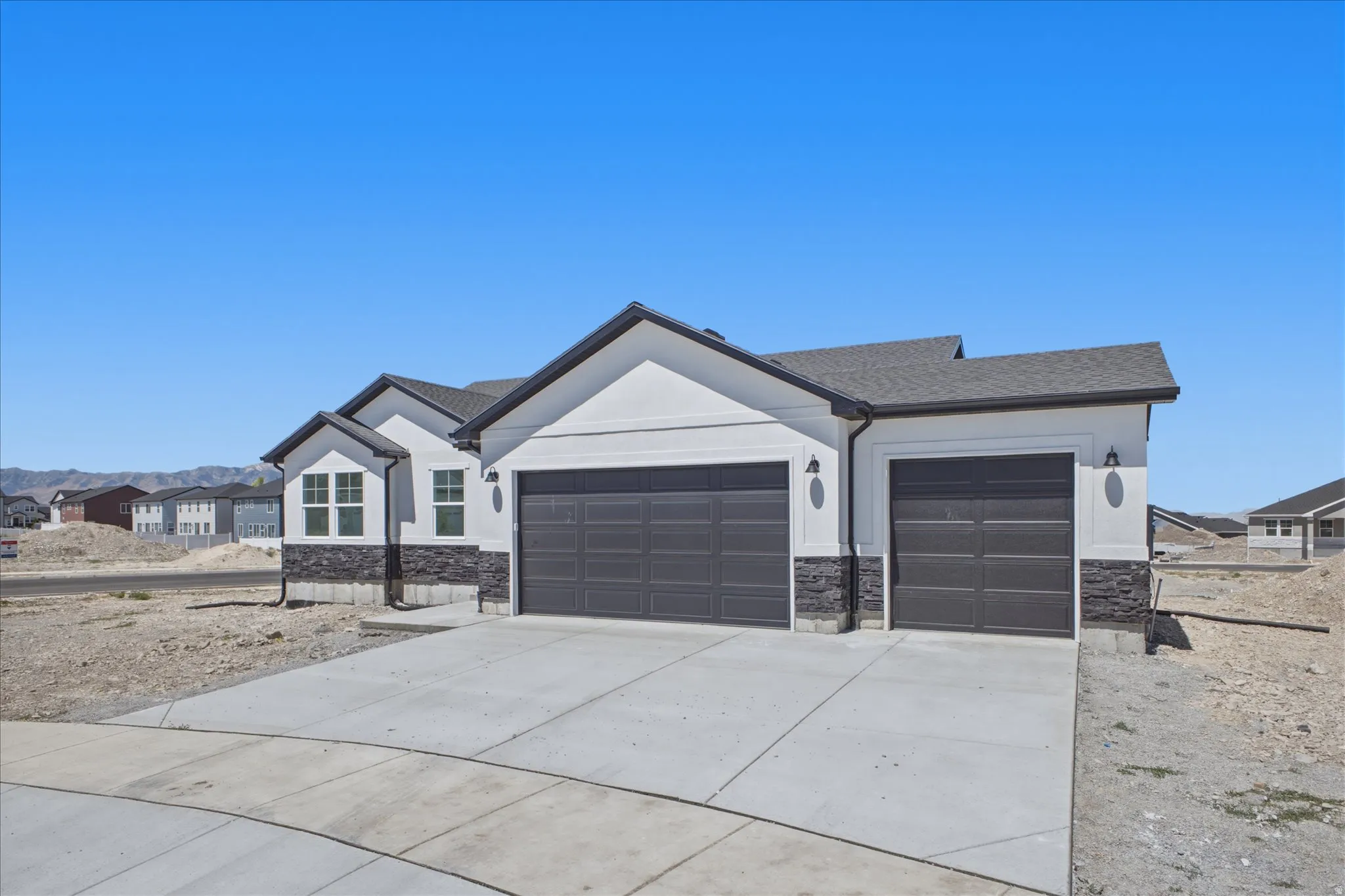 Contemporary exterior with light-colored siding and dark stone accent, featuring two dark garage doors and a concrete driveway