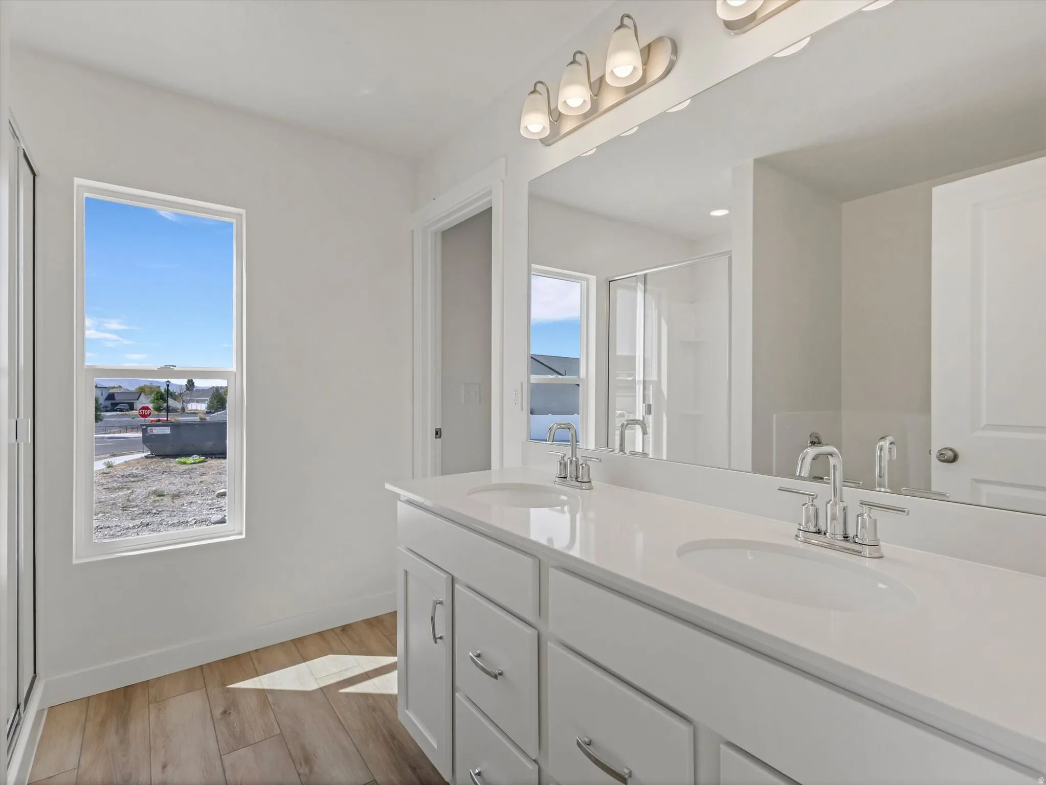 Dual vanity with white cabinetry, integrated sinks, chrome fixtures, and wood-finish flooring