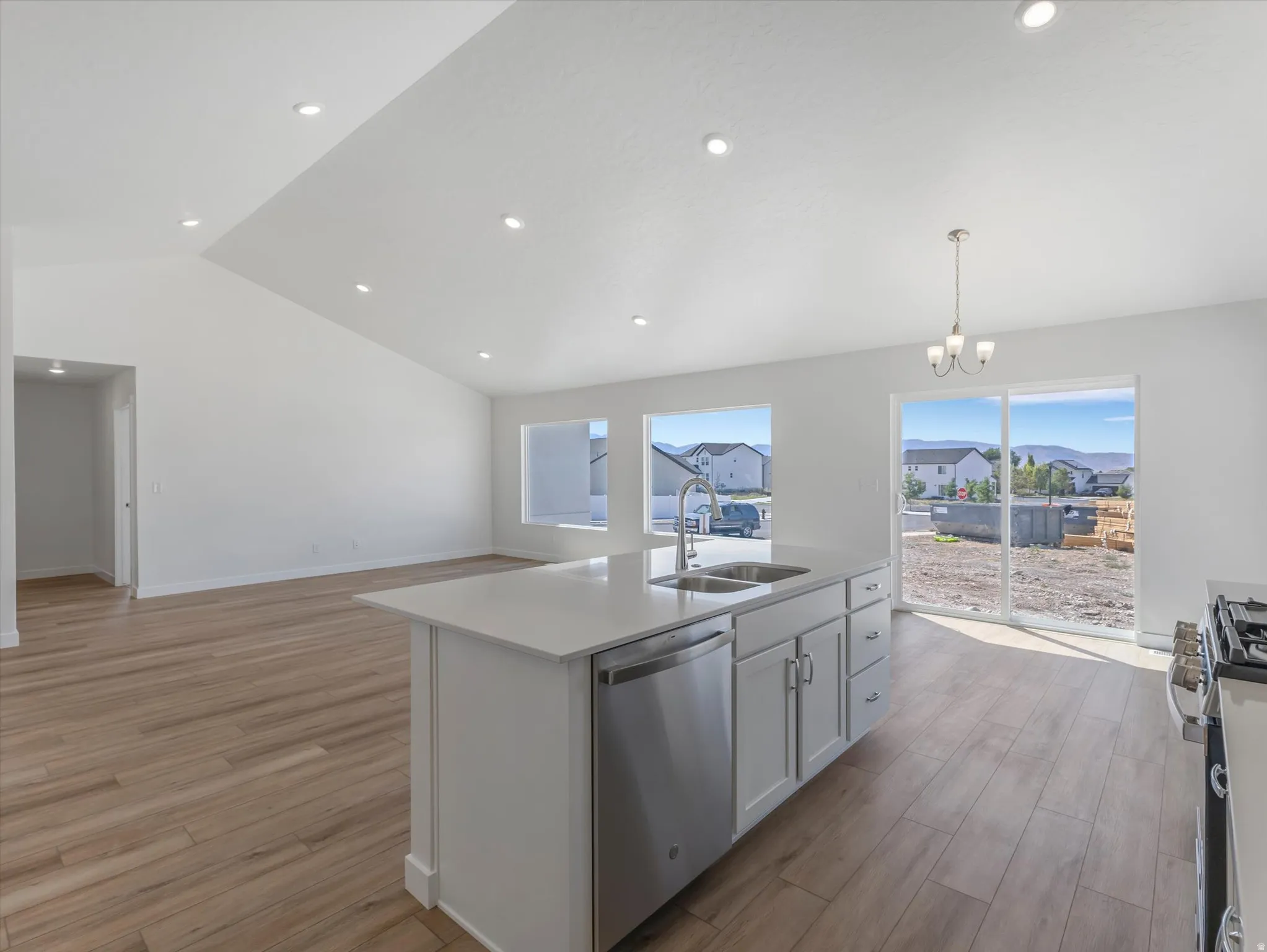 Vaulted ceilings with recessed lighting, wood-finish flooring, kitchen island with integrated sink, stainless steel dishwasher, and sliding glass door