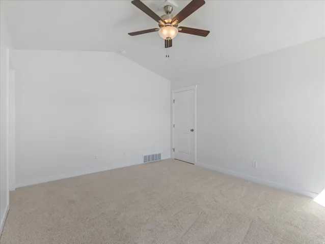 Textured carpet flooring, ceiling fan with integrated lighting, clean white walls, and a white door with dark hardware