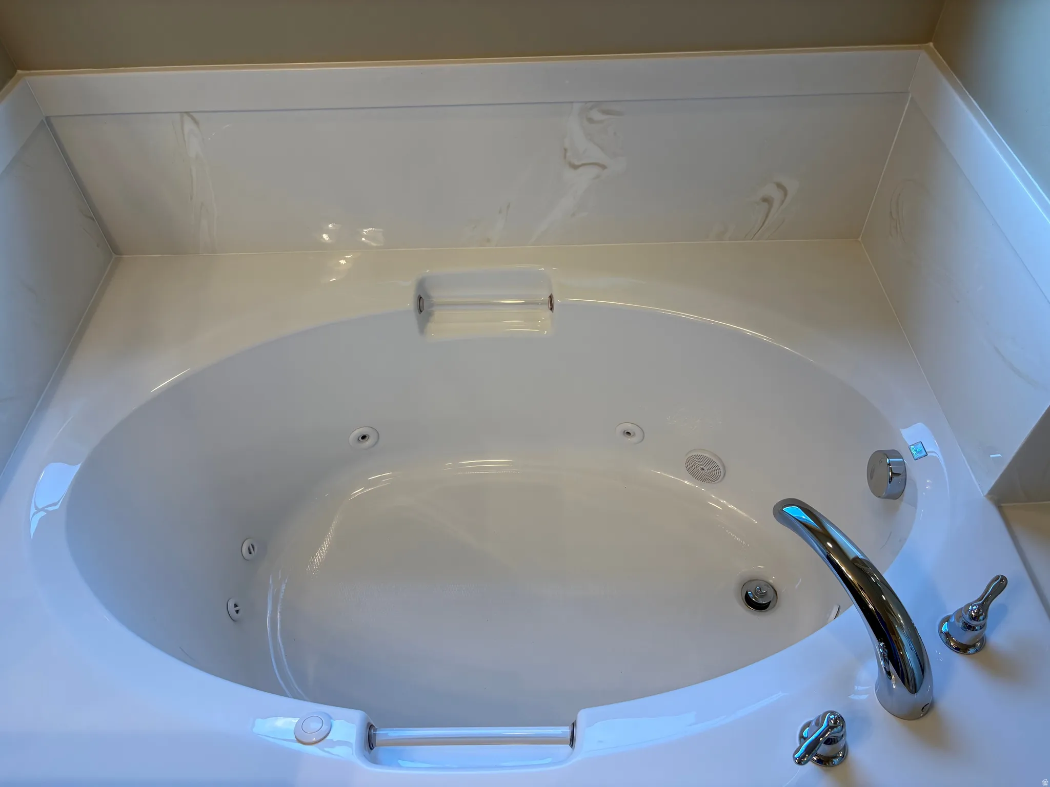 White acrylic jetted tub with integrated armrests, chrome fixtures, and a tiled surround
