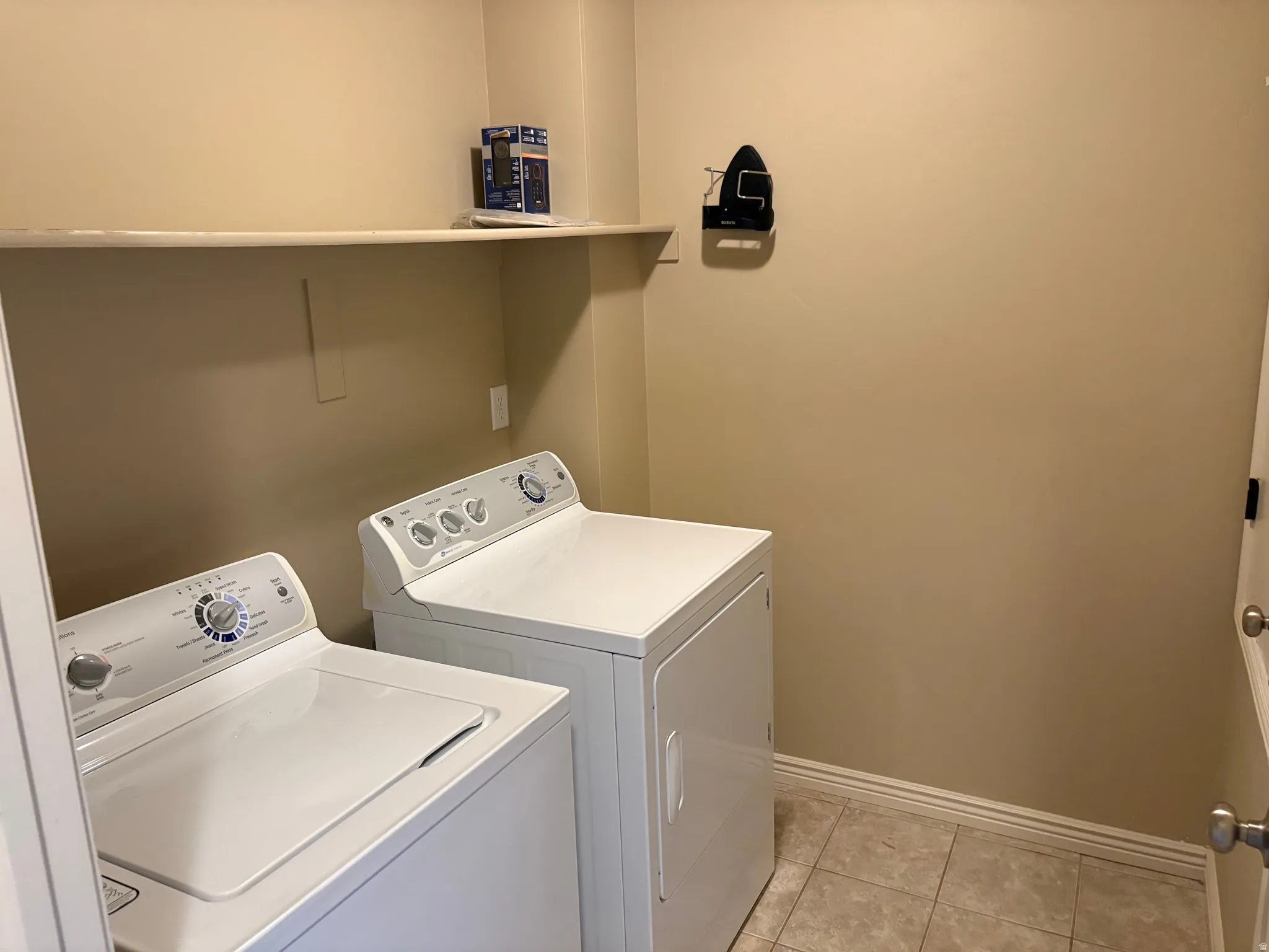 Dedicated laundry area featuring a washer and dryer, an overhead shelf, and tiled flooring