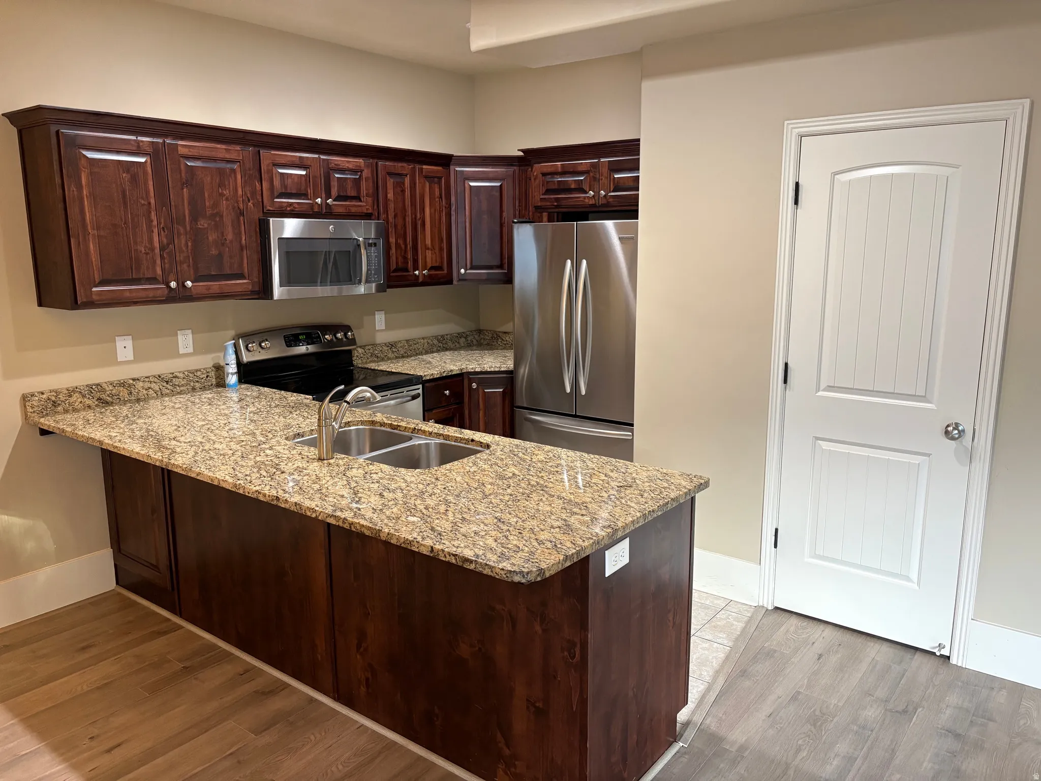 Kitchen featuring wood-finish cabinetry, granite countertops, stainless steel appliances, and wood-finish flooring