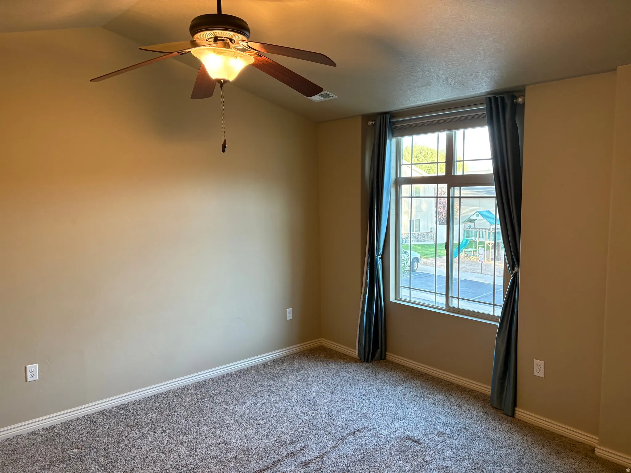 Neutral-toned carpeting, a window with grid patterns, and a ceiling fan with integrated lighting