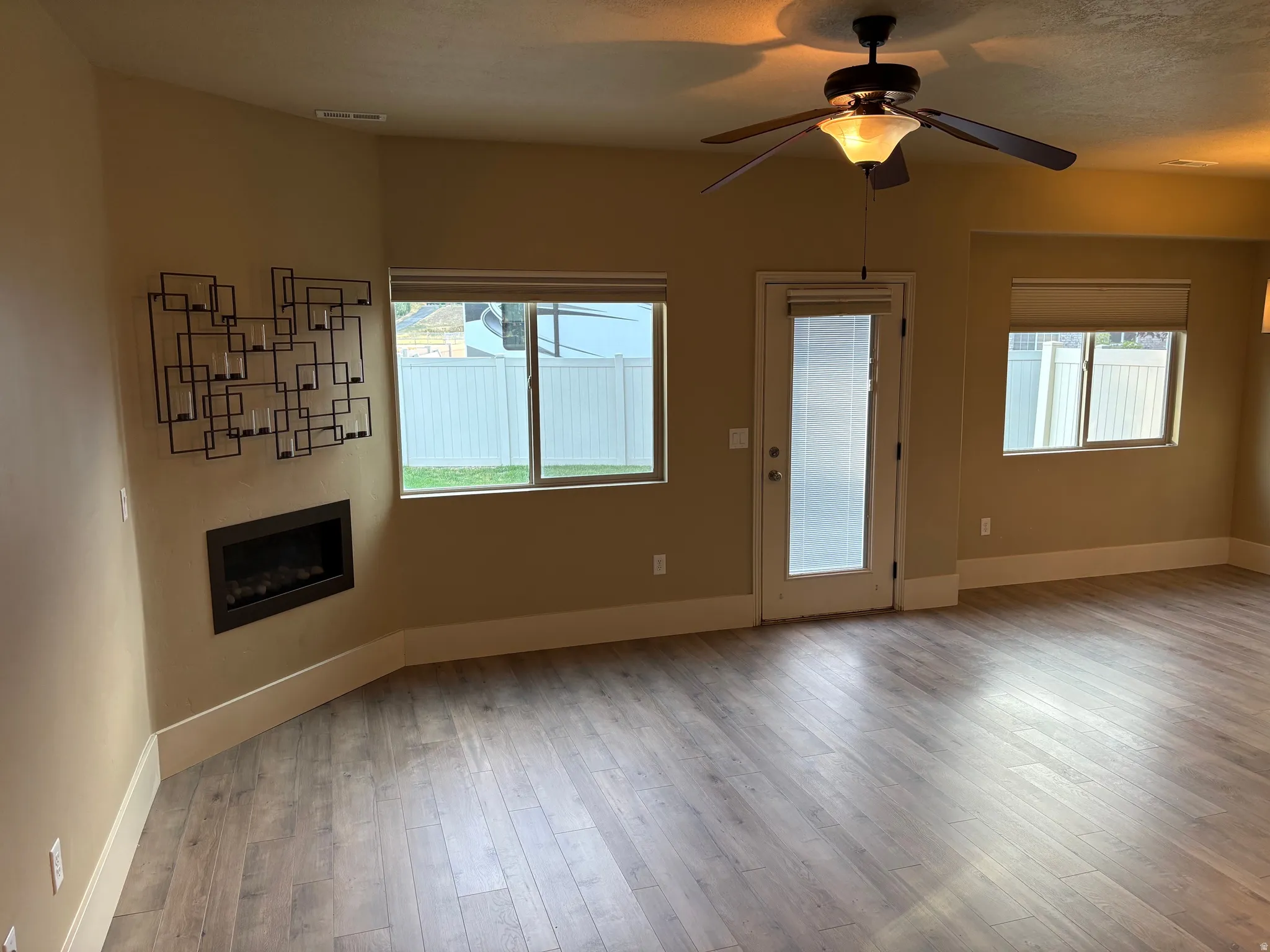 Wood-finish flooring throughout, featuring a built-in fireplace, multiple windows, and a ceiling fan with integrated lighting