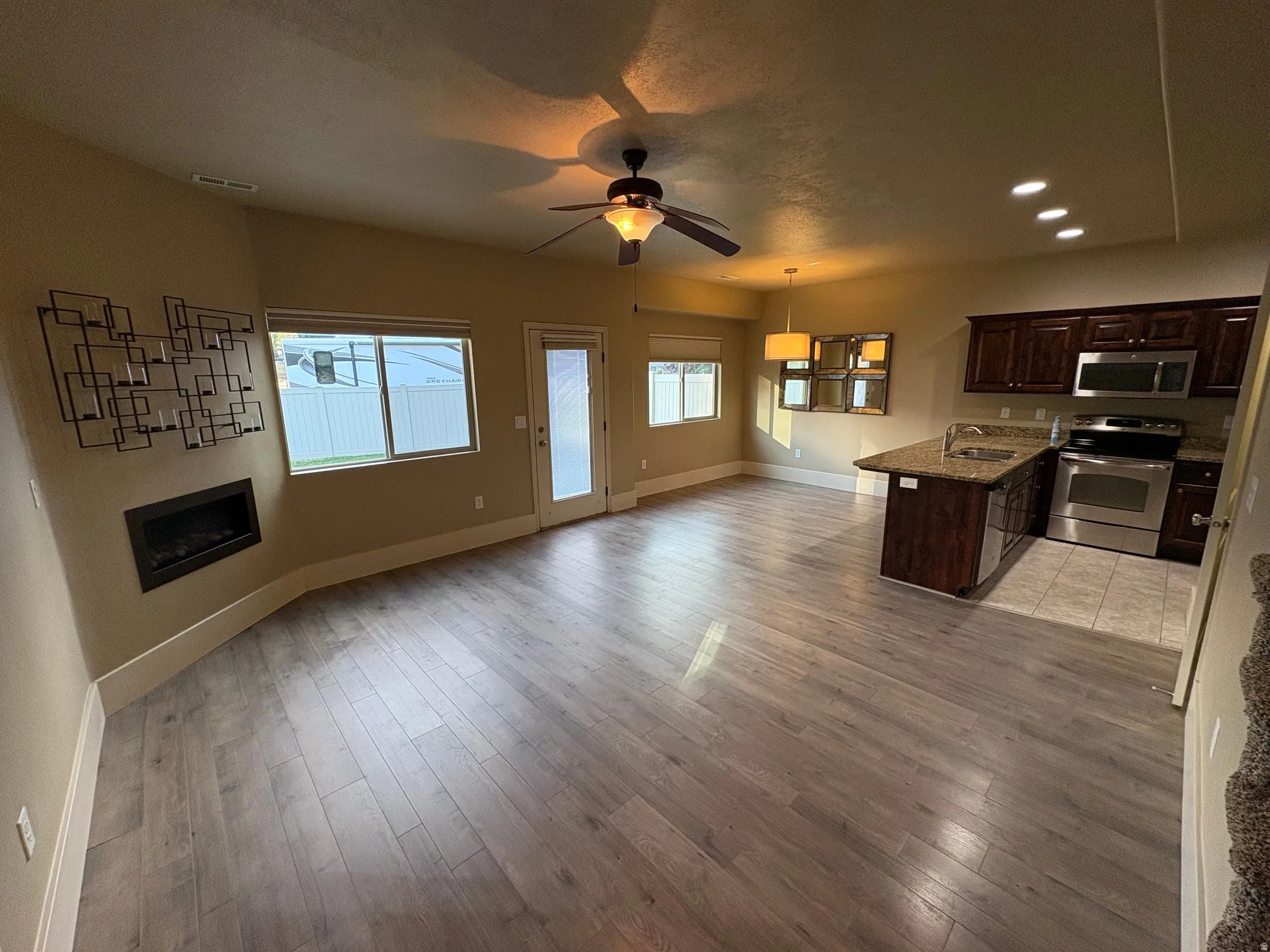 Spacious open-concept interior featuring wood-finish flooring, a built-in fireplace, and a ceiling fan with integrated lighting
