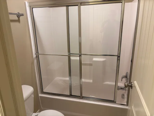 Bathtub with sliding glass shower doors, integrated seating, and chrome fixtures