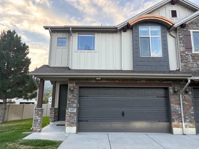 Stone and siding exterior with a dark gray garage door, featuring an arched window with decorative trim
