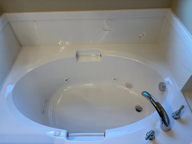 White acrylic jetted tub with integrated armrests, chrome fixtures, and a tiled surround