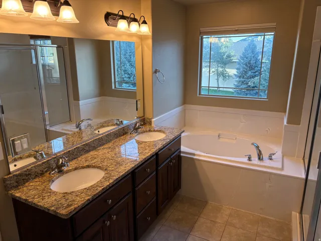 Dual vanity with granite countertops, an integrated soaking tub, tiled flooring, a large mirror, and a window with exterior views