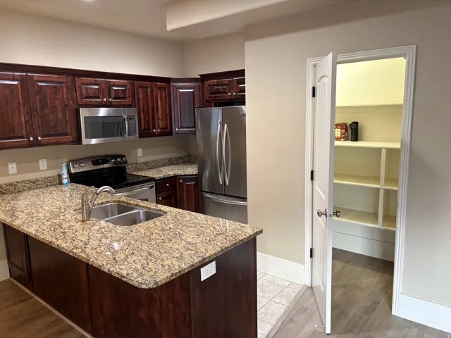 Kitchen featuring dark wood-finish cabinetry, stainless steel appliances, granite countertops, and a kitchen island with an undermount double-basin sink