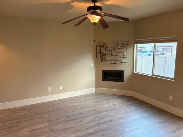 Wood-finish flooring, built-in electric fireplace, ceiling fan with integrated lighting, and a large window