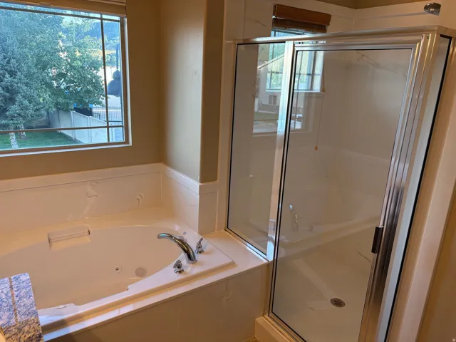 Jetted tub with chrome fixtures, glass-enclosed shower, and a large window