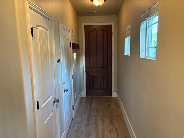 Wood-finish flooring with light-toned walls, featuring white paneled doors and a dark wood entry door