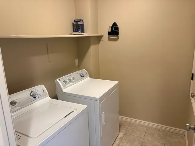 Dedicated laundry area featuring a washer and dryer, an overhead shelf, and tiled flooring