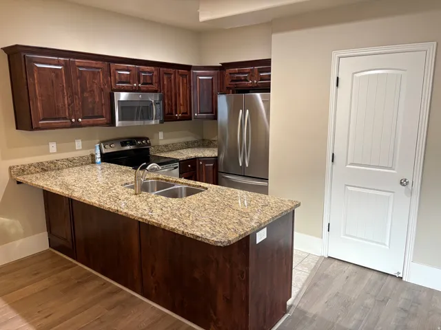 Kitchen featuring wood-finish cabinetry, granite countertops, stainless steel appliances, and wood-finish flooring