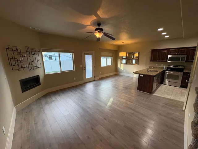 Spacious open-concept interior featuring wood-finish flooring, a built-in fireplace, and a ceiling fan with integrated lighting