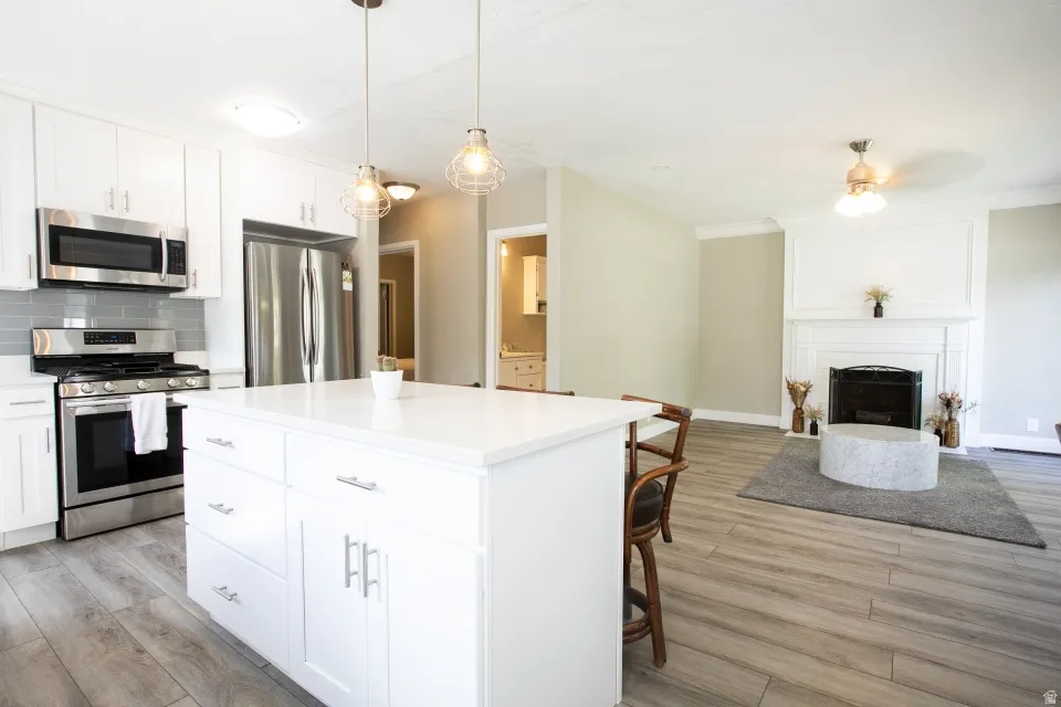Modern kitchen with stainless steel appliances, white cabinetry, a center island with pendant lighting, and wood-finish flooring