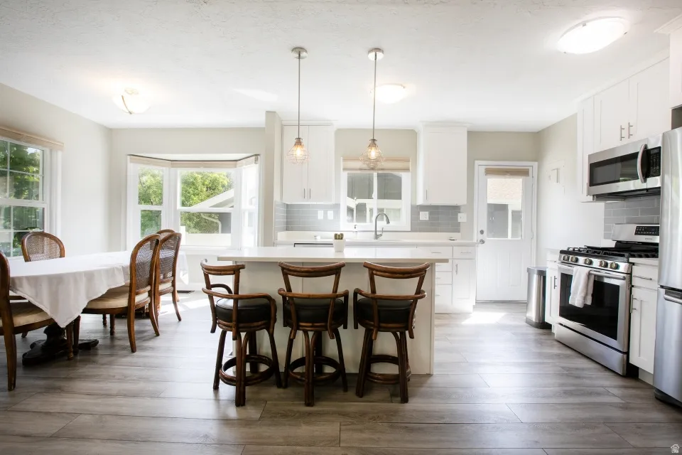 White cabinetry kitchen featuring stainless steel appliances, a center island with pendant lighting, a tile backsplash, and wood-finish flooring