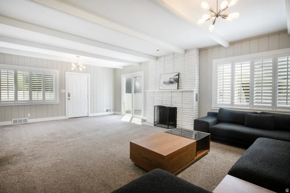Exposed ceiling beams, white painted brick fireplace, white paneling, white plantation shutters, and a sliding glass door
