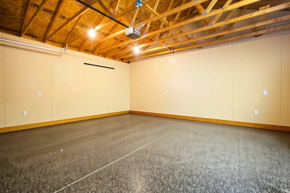 Exposed wood ceiling joists, overhead lighting, finished wall panels, and a concrete floor