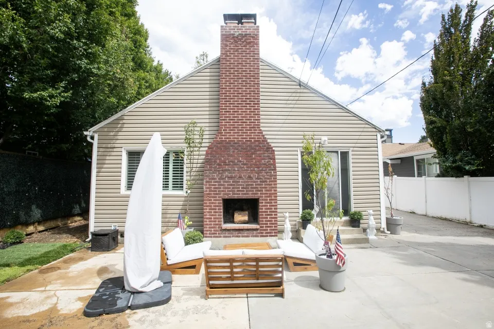 Exterior siding, brick chimney, concrete patio, sliding glass door, and mature trees