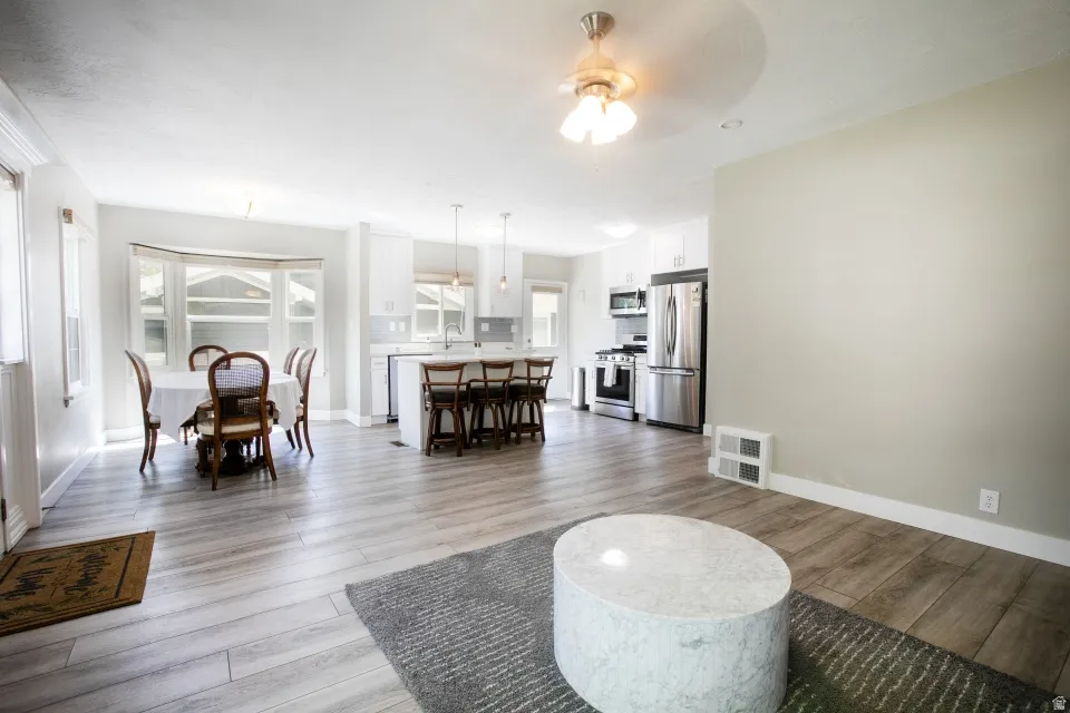 Open-concept living space featuring wood-finish flooring, a bay window, a kitchen island with seating, pendant lighting, and stainless steel appliances