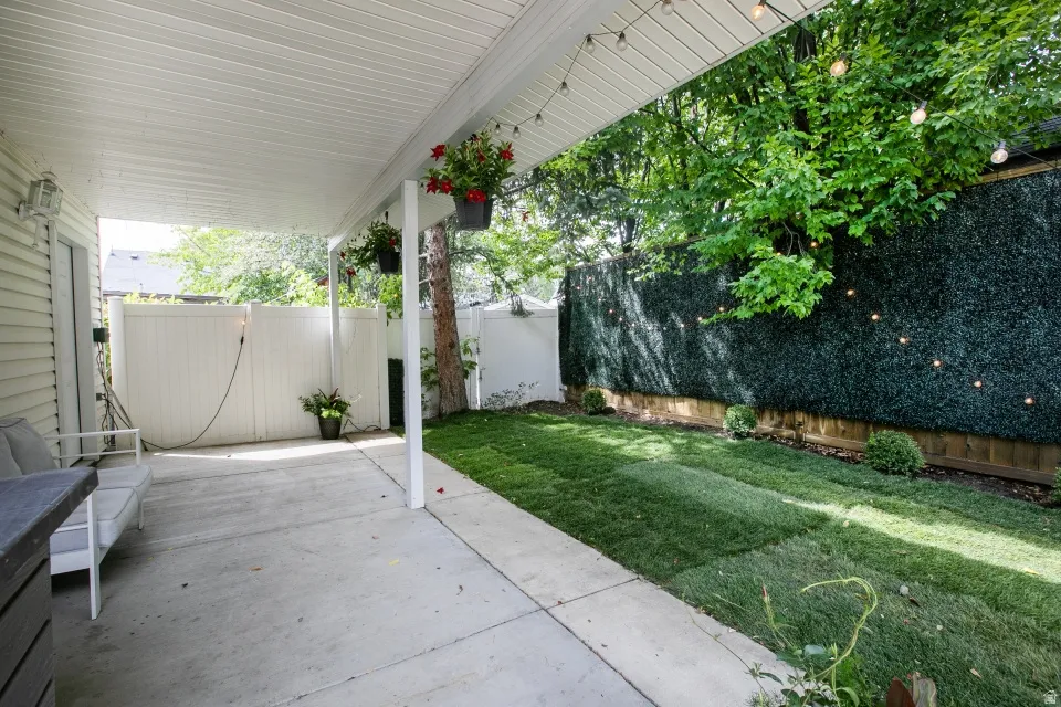 Covered patio with concrete flooring, accompanied by a manicured lawn and privacy fencing
