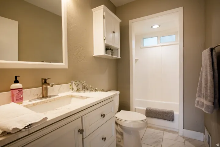 Bathroom featuring a vanity with an integrated sink, a wall-mounted mirror, a built-in shower/tub combination, and a white storage cabinet