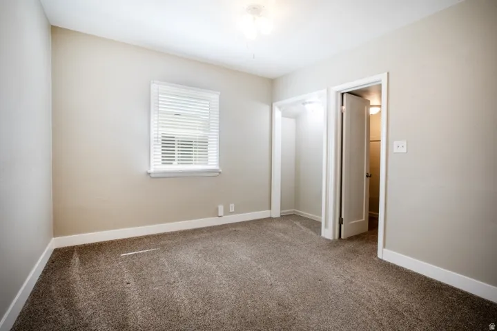 Neutral-toned walls, carpeted flooring, window with blinds, cased doorway, and an open closet space