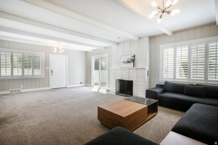 Exposed ceiling beams, white painted brick fireplace, white paneling, white plantation shutters, and a sliding glass door